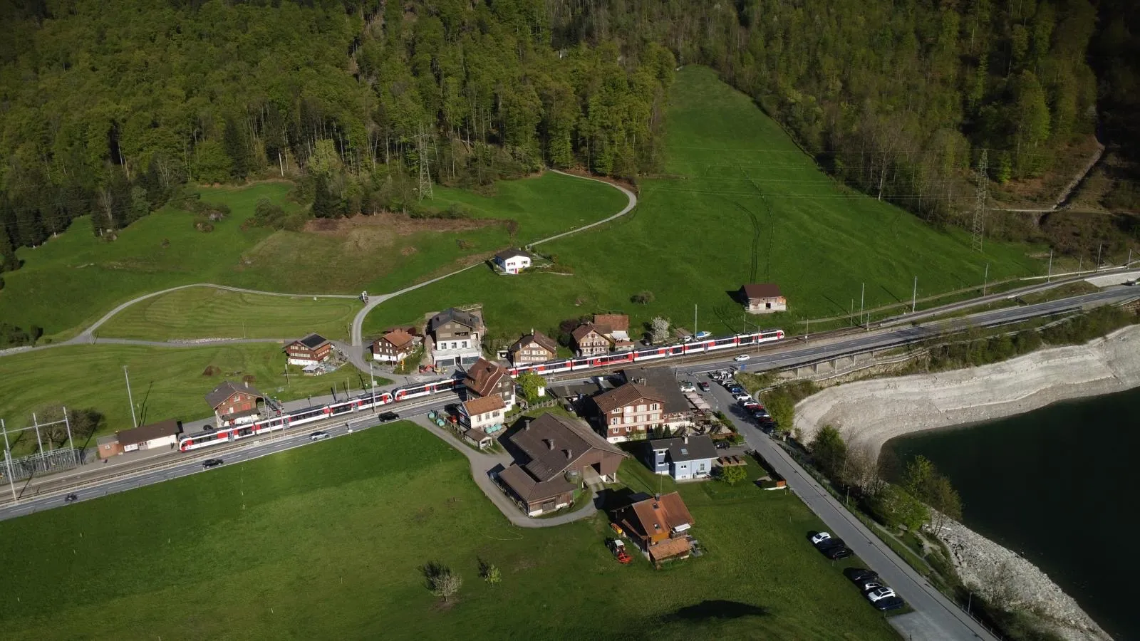 Dorf mit Bahnlinie zwischen Wiesen und Wald von oben